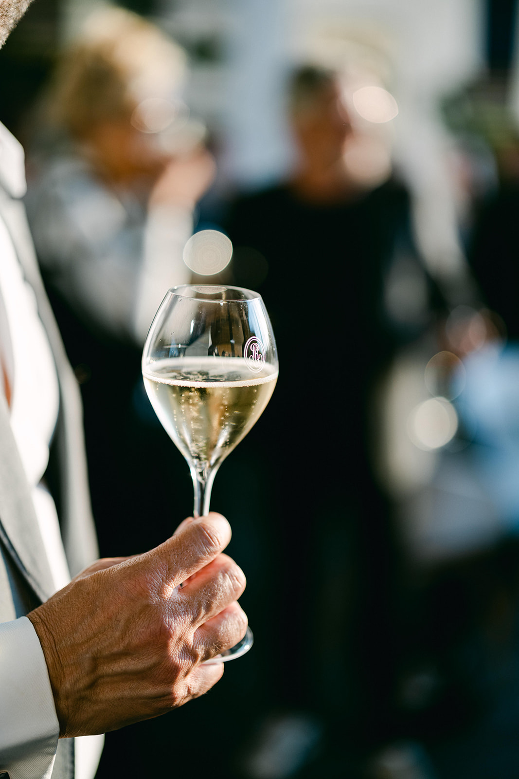 eine Hand hält ein Roederer Champagnerglas in der Hand in die Sonne