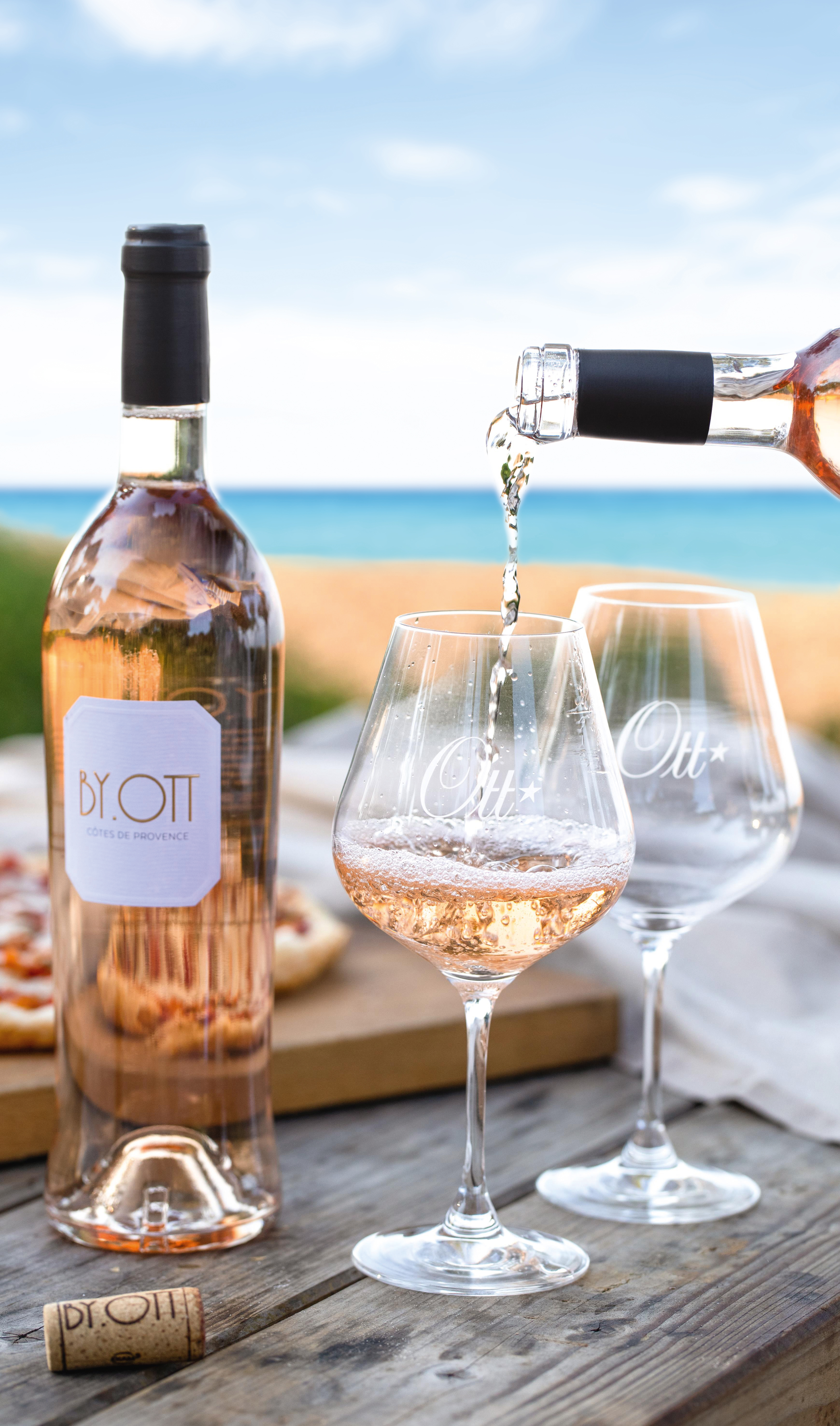 Eine Flasche Rose BY OTT steht auf einem Tisch, daneben zwei Gläser und in eins davon wird Rosewein eingeschenkt